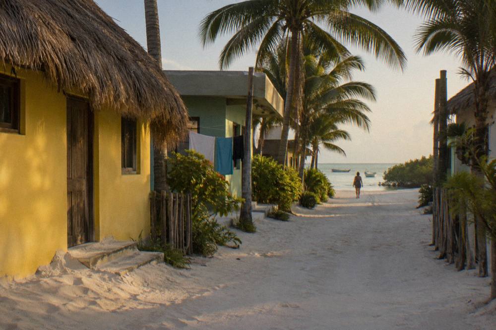 Colourful painted houses along a sandy lane in Holbox village in early morning light